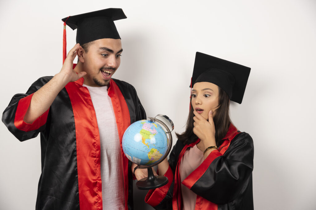 pair happy in graduation gowns carrying a globe and looking at the globe