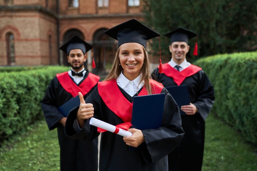 graduate female shows like with her friends graduation gowns holding certificate smiling camera